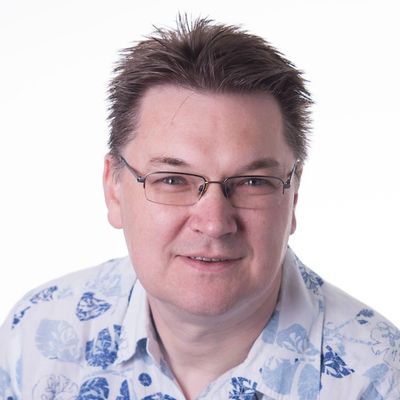 Middle-age white man with squarish face and short brown straight hair. Man is wearing glasses and has a short sleeved white shirt with a light and dark blue leaf pattern printed on it